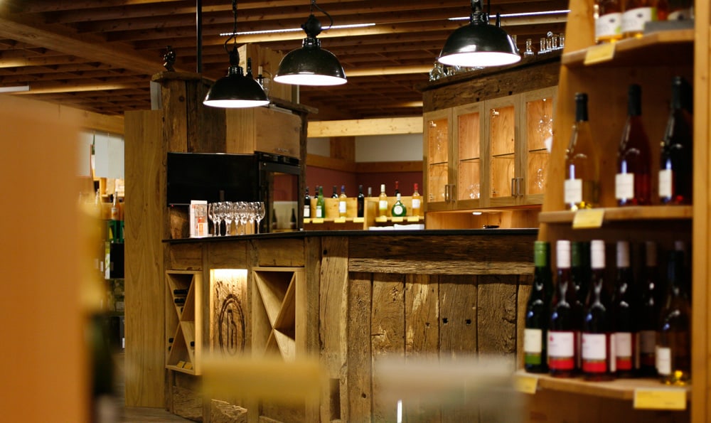 Innenansicht eines rustikalen Weinladens mit Holztheke, hängenden Lampen und Regalen voller Weinflaschen.