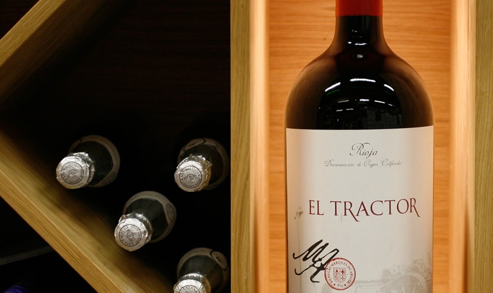 Eine Flasche Rotwein "El Tractor" mit anderen Weinflaschen in einem Holzregal.